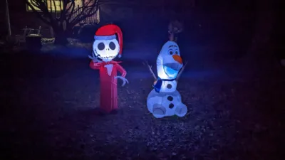 A nightime picture of two inflatable holiday decorations. Jack skellington dressed as Santa and a sitting Olaf.